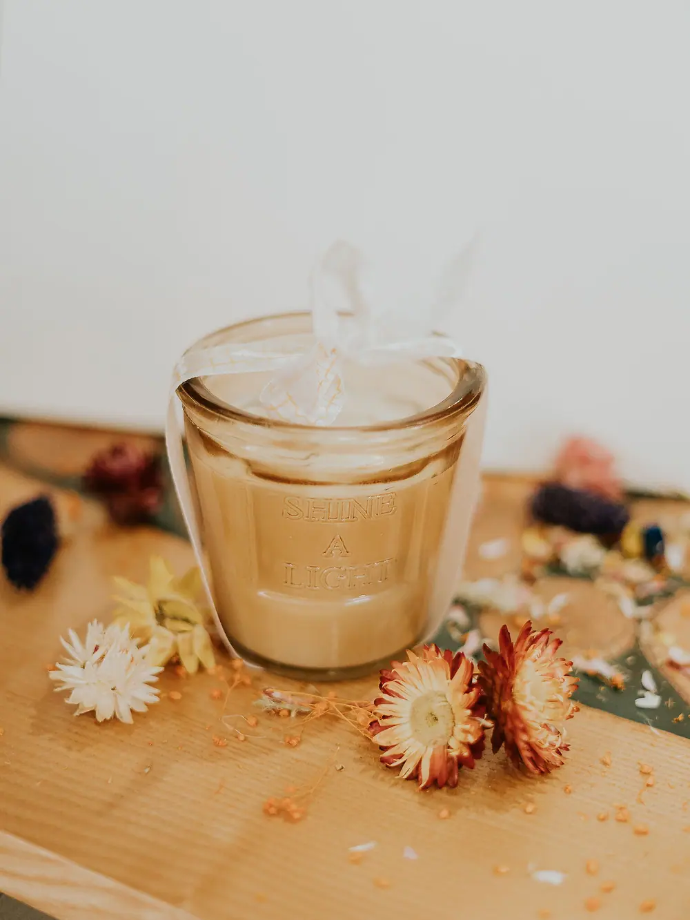 Bougie ambrée entourée de fleurs séchées sur un plan de bois