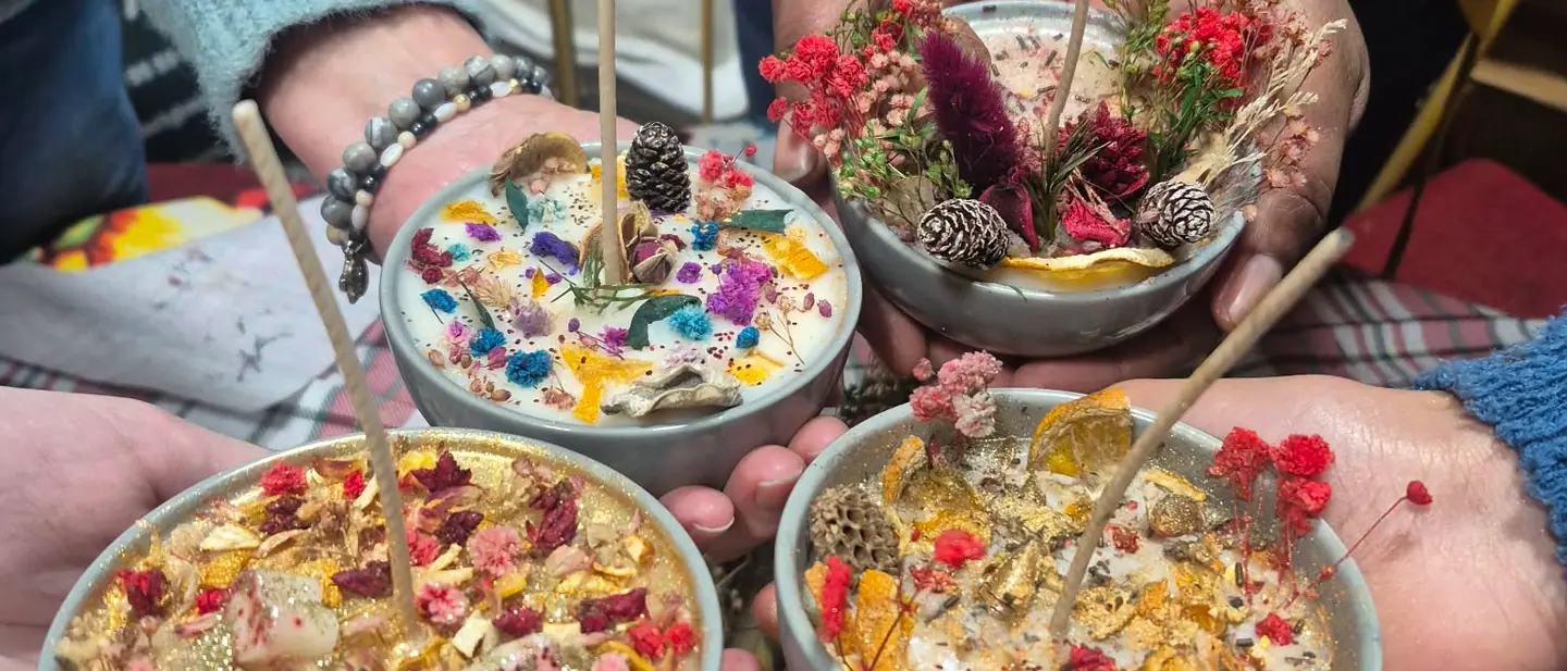 Quatre paires de mains présentant les bougies décorées de fleurs séchées réalisées en atelier