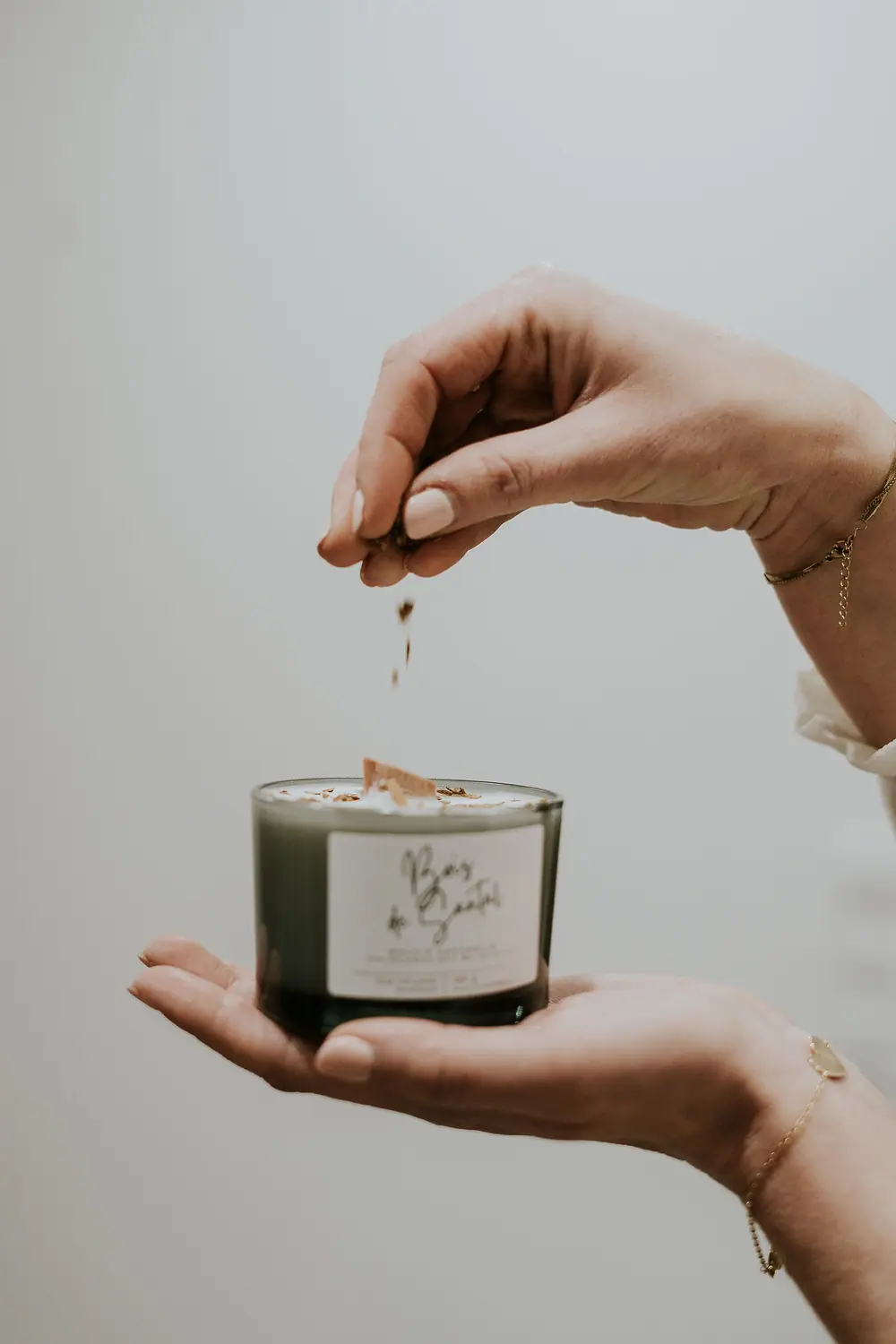 Bougie parfumée ambrée entourée de fleurs séchées sur un plan de bois clair